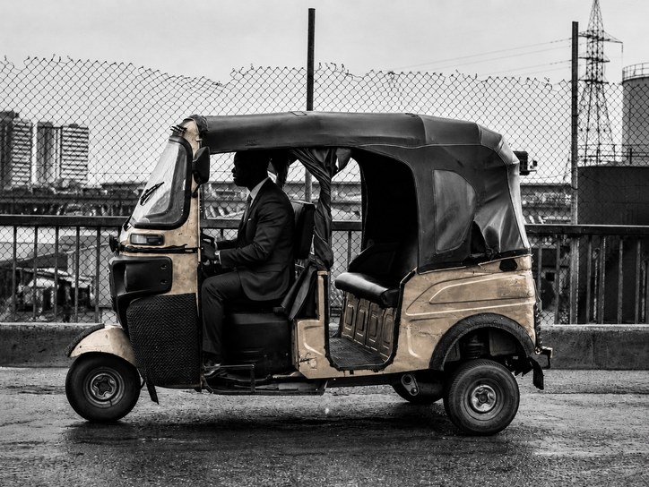 A suited passenger travelling by keke past the Lagos skyline